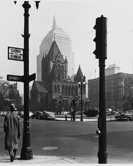 Who's The Father — vintage black-and-white street view with a European cathedral rising in the background.